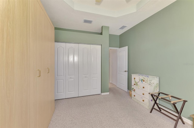 bedroom featuring light colored carpet, a raised ceiling, and a closet