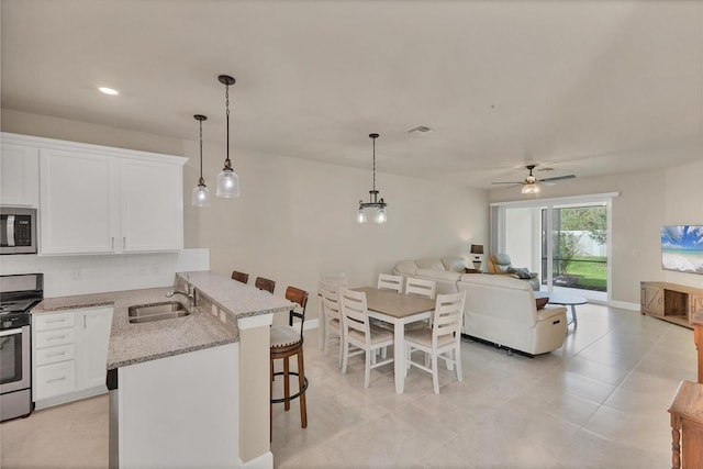 kitchen with hanging light fixtures, sink, appliances with stainless steel finishes, white cabinets, and a kitchen bar