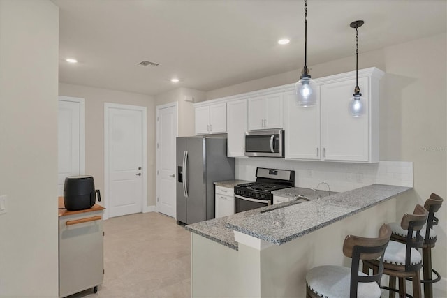 kitchen featuring hanging light fixtures, a breakfast bar, backsplash, appliances with stainless steel finishes, and white cabinets