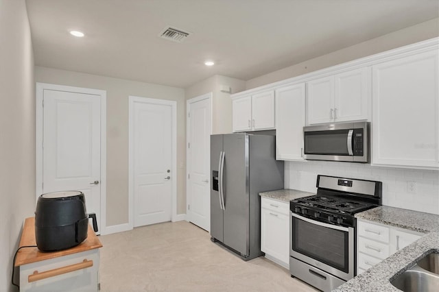 kitchen with white cabinetry, backsplash, appliances with stainless steel finishes, and light stone countertops