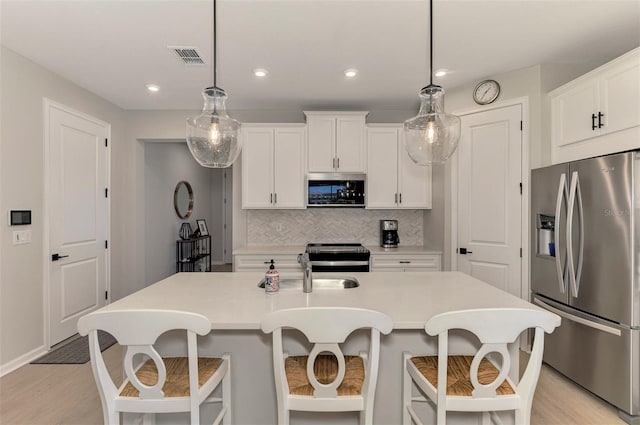 kitchen with pendant lighting, stainless steel appliances, tasteful backsplash, light countertops, and white cabinets