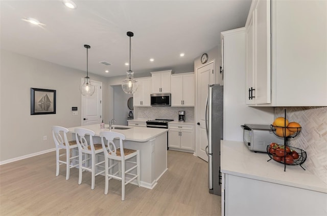 kitchen with stainless steel appliances, a sink, white cabinetry, light wood-style floors, and an island with sink