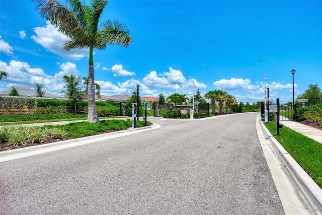 view of road with sidewalks, curbs, a gated entry, and street lights