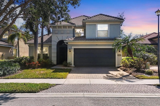 mediterranean / spanish-style home featuring an attached garage, a tile roof, decorative driveway, and stucco siding