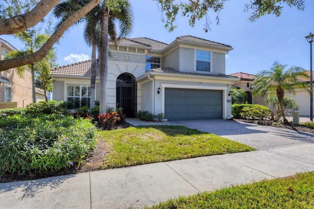 mediterranean / spanish house with a garage, a tiled roof, decorative driveway, and stucco siding