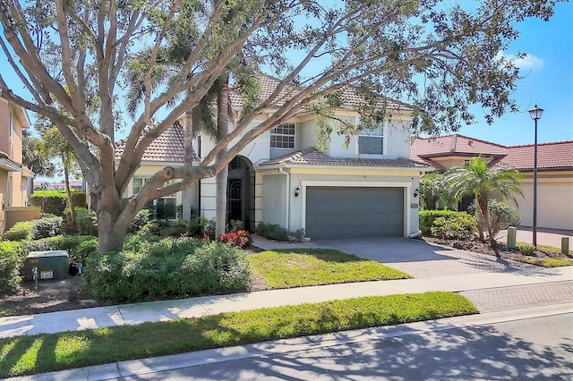 mediterranean / spanish home with a tiled roof, decorative driveway, an attached garage, and stucco siding