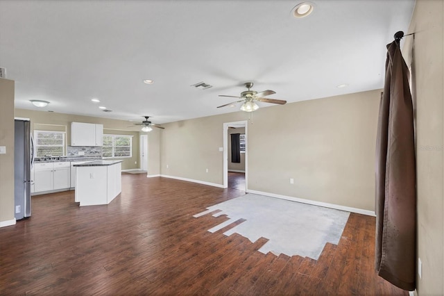 unfurnished living room featuring dark wood-type flooring, visible vents, ceiling fan, and baseboards