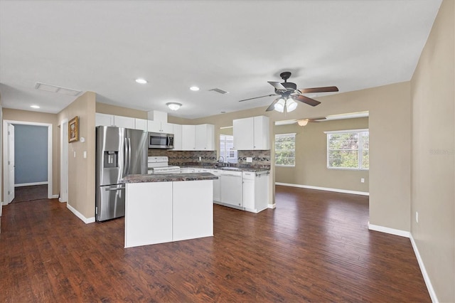 kitchen featuring dark countertops, a center island, stainless steel appliances, white cabinetry, and backsplash