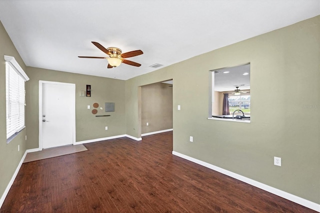 interior space with dark wood-type flooring, a ceiling fan, visible vents, and baseboards