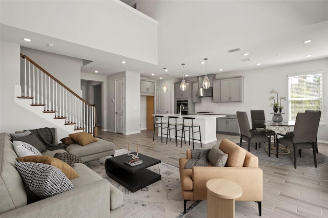 living room featuring a towering ceiling, light wood-style flooring, stairs, and recessed lighting