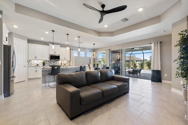 living room featuring visible vents, baseboards, a tray ceiling, light tile patterned floors, and a ceiling fan