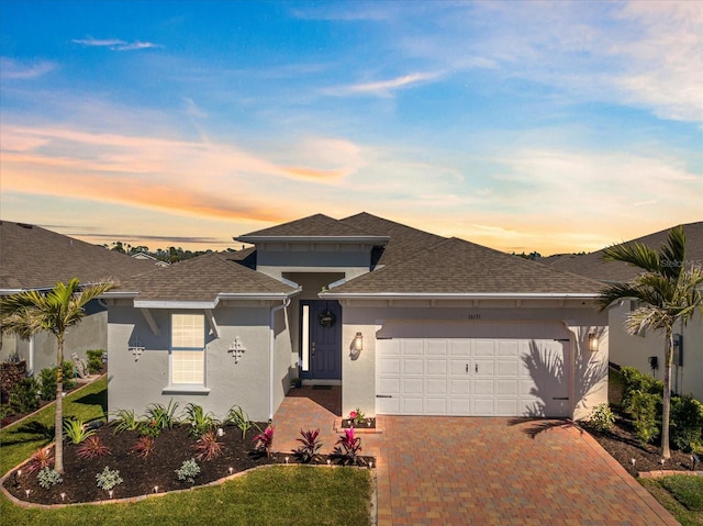 view of front of house with decorative driveway, roof with shingles, an attached garage, and stucco siding