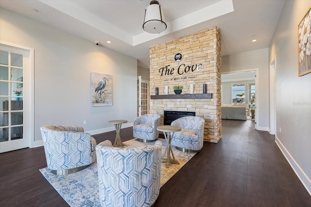 living room featuring a raised ceiling, wood finished floors, recessed lighting, a stone fireplace, and baseboards