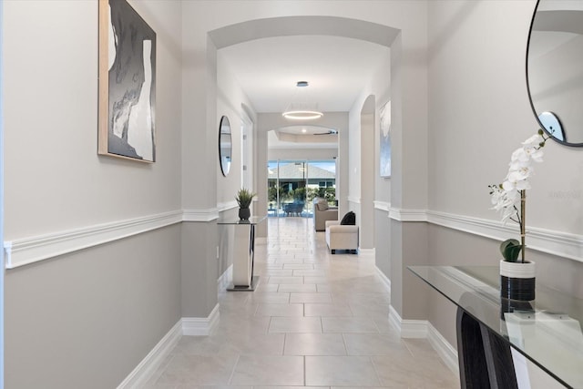 corridor with light tile patterned floors, arched walkways, and baseboards