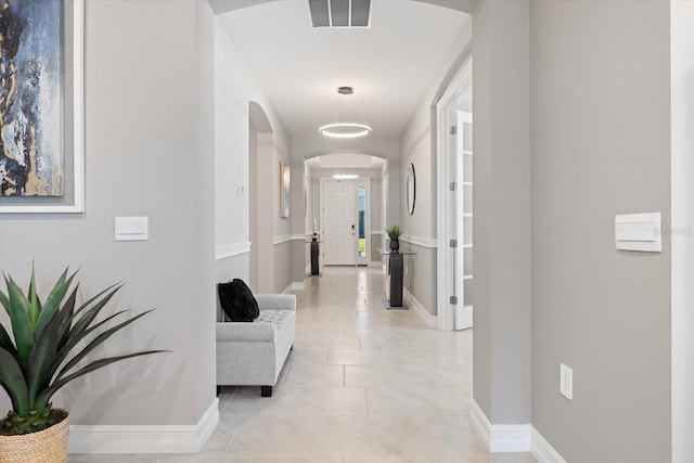 hallway with light tile patterned floors, arched walkways, visible vents, and baseboards