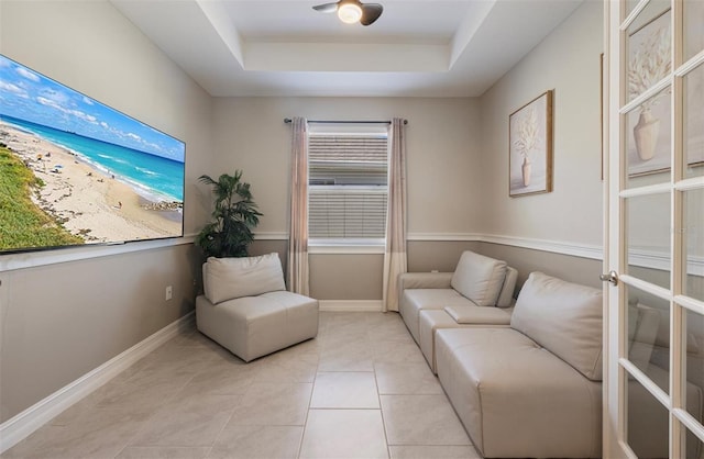 sitting room with light tile patterned floors, a raised ceiling, and baseboards