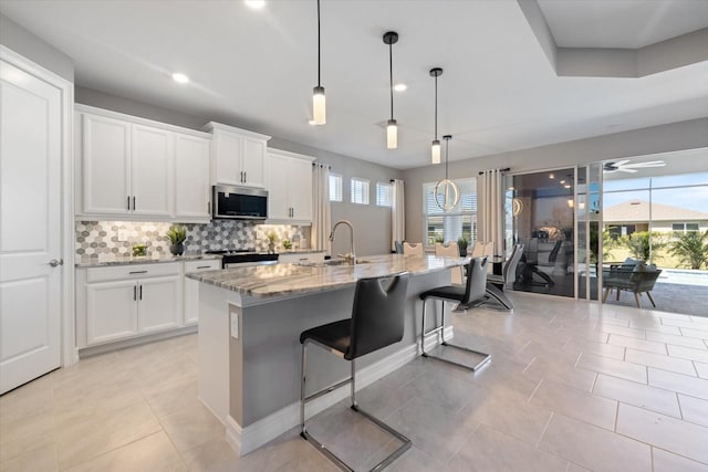 kitchen featuring a sink, light stone counters, tasteful backsplash, white cabinetry, and stainless steel appliances