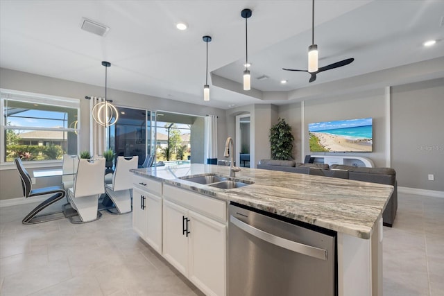 kitchen with a center island with sink, dishwasher, a tray ceiling, light stone counters, and a sink