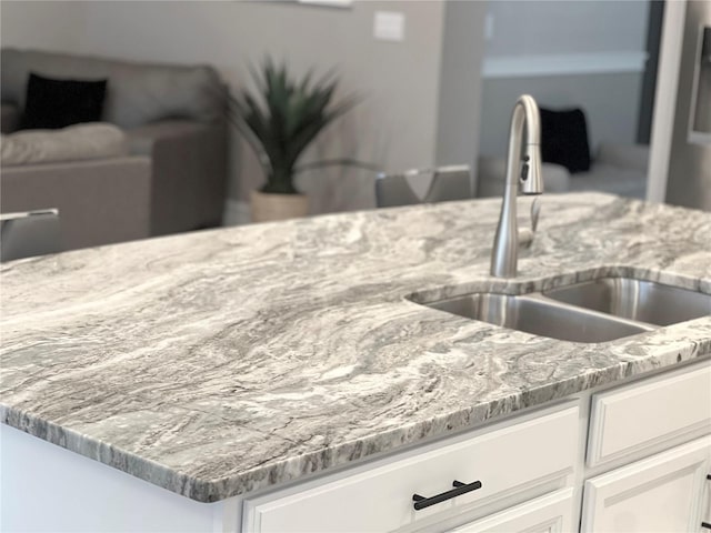 interior details featuring a sink, light stone countertops, and white cabinetry