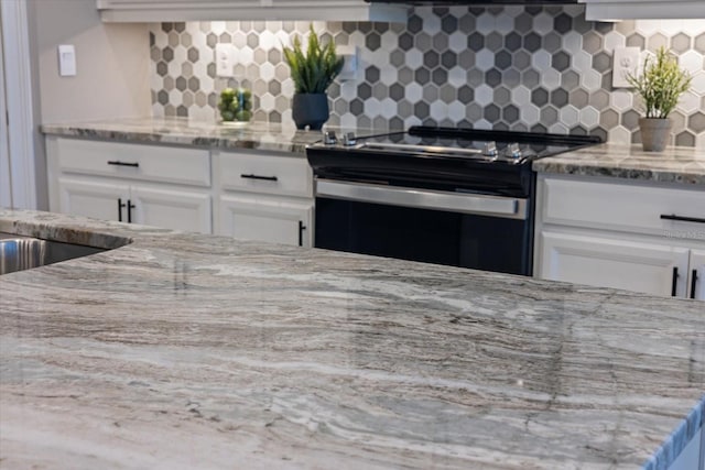 kitchen with backsplash, range with electric stovetop, white cabinets, and light stone countertops