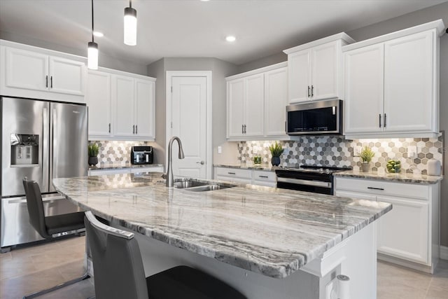 kitchen with a breakfast bar, a kitchen island with sink, a sink, stainless steel appliances, and white cabinets