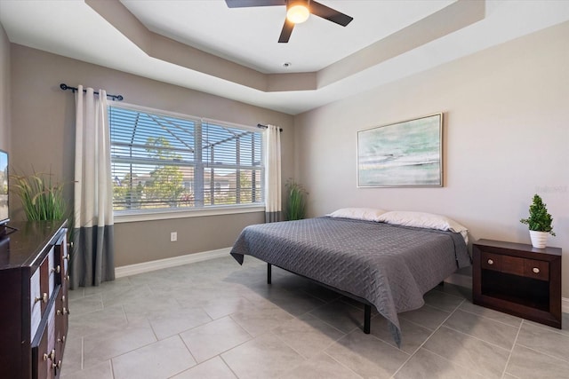 bedroom featuring light tile patterned floors, baseboards, a raised ceiling, and a ceiling fan