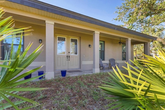 view of exterior entry featuring a porch, a ceiling fan, and stucco siding