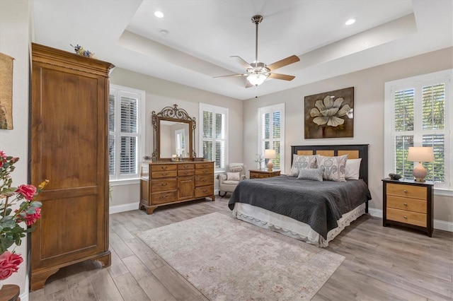 bedroom featuring light wood-type flooring, a raised ceiling, and baseboards