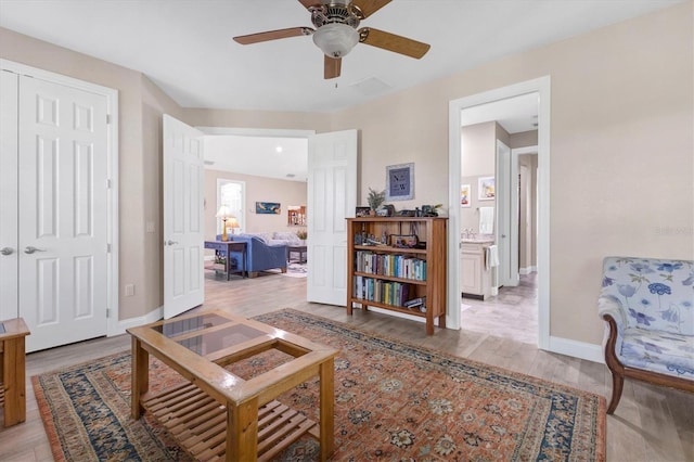 living area with baseboards, a ceiling fan, and light wood finished floors