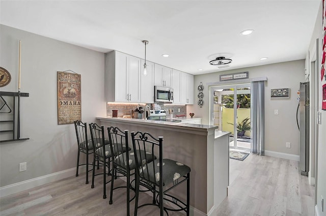 kitchen with white cabinets, decorative backsplash, appliances with stainless steel finishes, a peninsula, and a kitchen bar