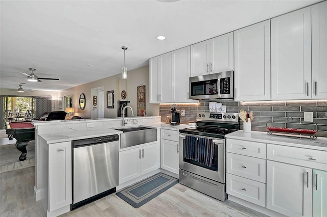 kitchen featuring stainless steel appliances, white cabinets, a sink, and a peninsula