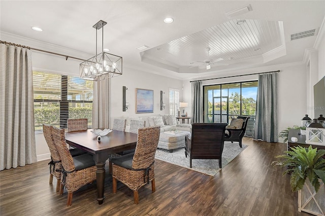 dining space with a tray ceiling, visible vents, ornamental molding, wood finished floors, and ceiling fan with notable chandelier