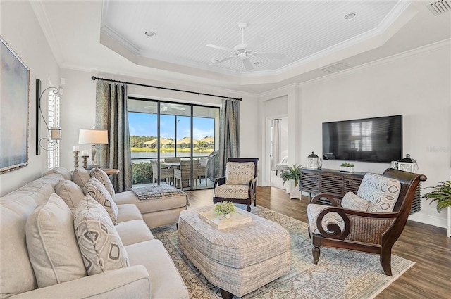 living area featuring baseboards, visible vents, a raised ceiling, wood finished floors, and crown molding