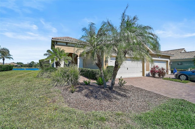 view of front of home with decorative driveway, stucco siding, a garage, a tiled roof, and a front lawn