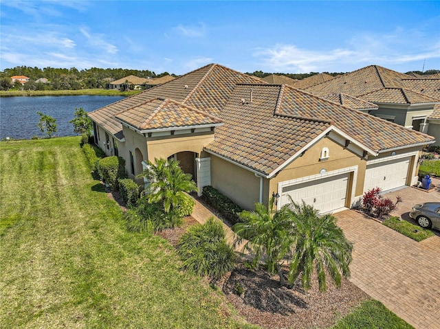 mediterranean / spanish-style home featuring stucco siding, a water view, decorative driveway, a garage, and a tiled roof