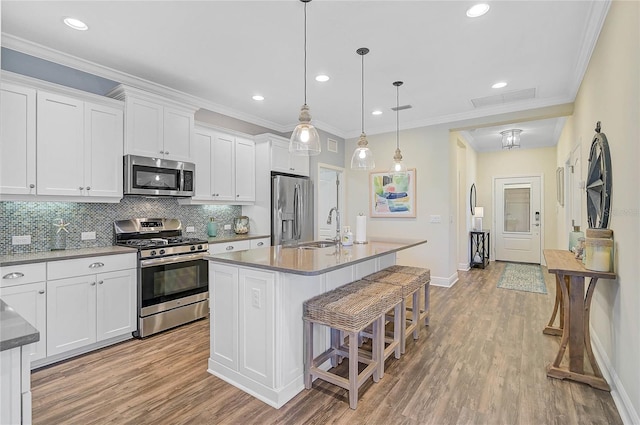 kitchen with stainless steel appliances, backsplash, white cabinets, a sink, and an island with sink