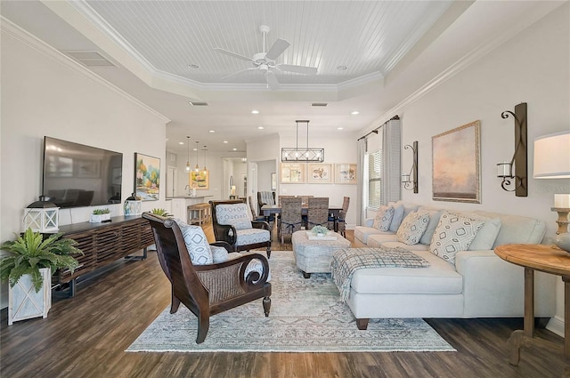 living room with visible vents, wood finished floors, a tray ceiling, crown molding, and ceiling fan with notable chandelier