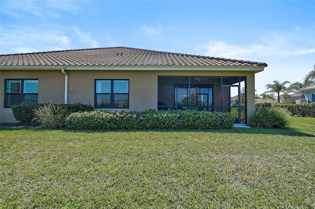 back of house with a sunroom, a tiled roof, stucco siding, and a yard