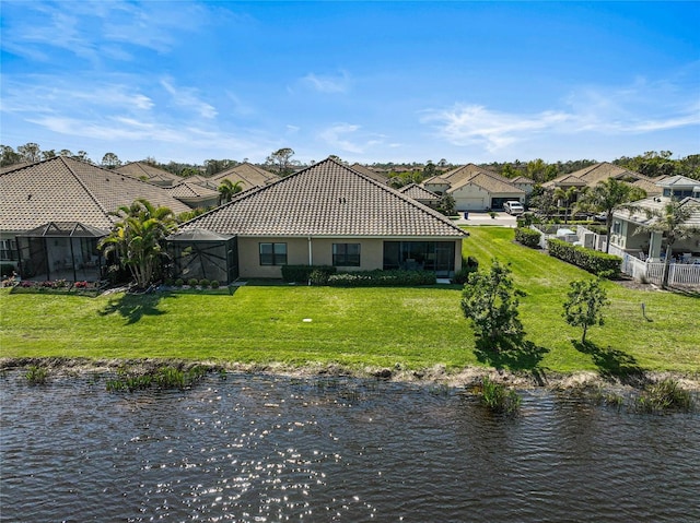 rear view of property with a water view, a yard, a tiled roof, and stucco siding