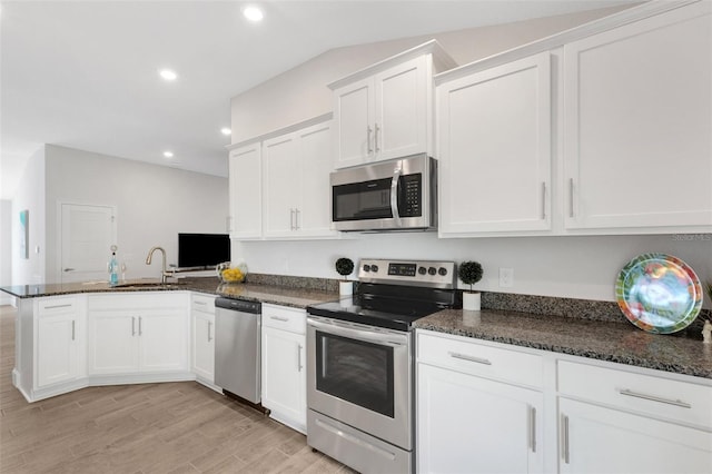 kitchen featuring appliances with stainless steel finishes, dark stone countertops, a peninsula, white cabinetry, and a sink