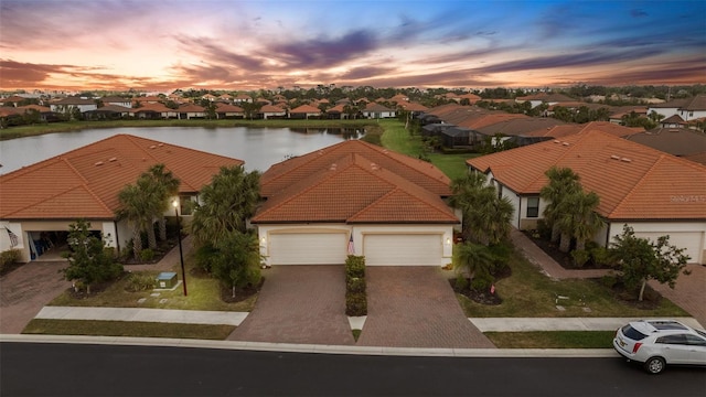 aerial view at dusk featuring a water view and a residential view