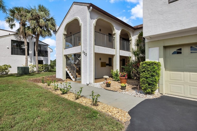 view of exterior entry featuring a garage, a yard, a balcony, and stucco siding