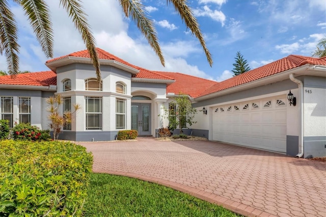 mediterranean / spanish-style home with a tiled roof, french doors, decorative driveway, and an attached garage