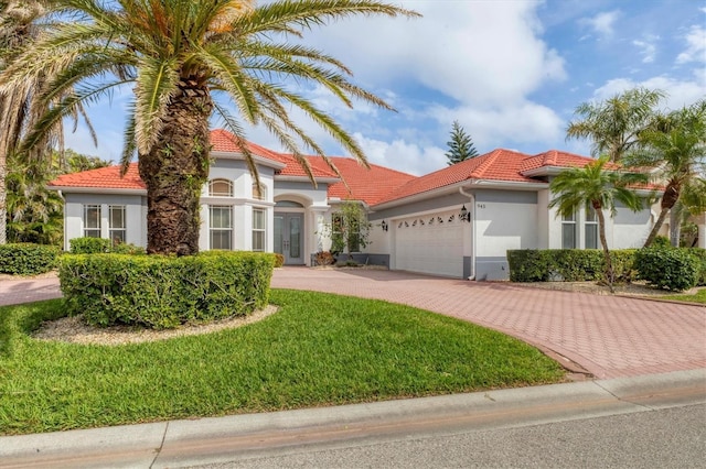 mediterranean / spanish house featuring an attached garage, a tile roof, decorative driveway, stucco siding, and a front lawn