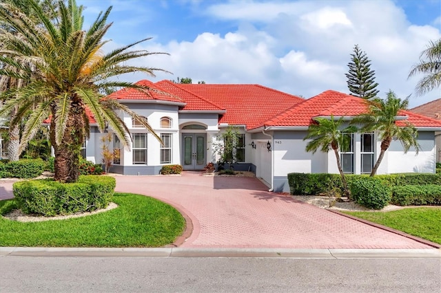 mediterranean / spanish house with stucco siding, a tiled roof, decorative driveway, and french doors