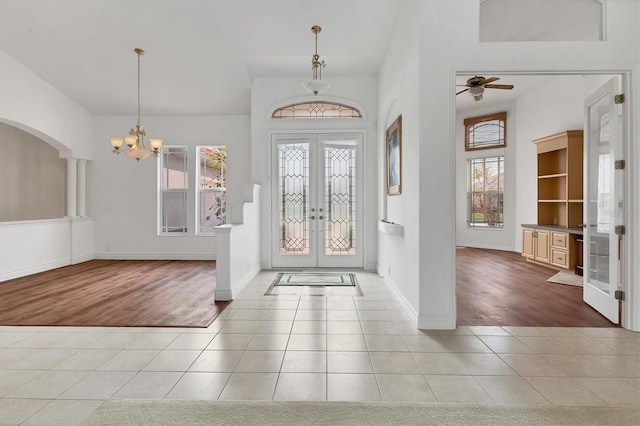 entrance foyer featuring baseboards, arched walkways, tile patterned flooring, french doors, and ceiling fan with notable chandelier