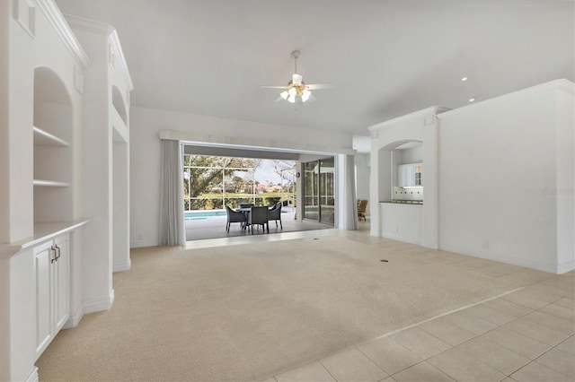 unfurnished living room featuring a ceiling fan, a sunroom, light carpet, light tile patterned flooring, and baseboards