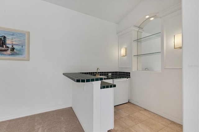 kitchen with baseboards, tile counters, white cabinets, a peninsula, and a kitchen bar