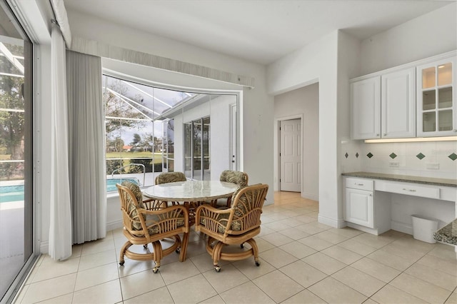 dining area with a sunroom, built in desk, baseboards, and light tile patterned floors