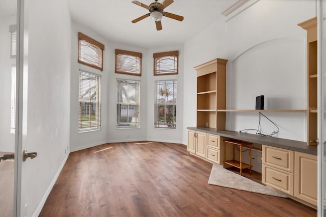 unfurnished office featuring ceiling fan, built in desk, baseboards, and wood finished floors